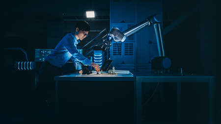 Japanese Development Engineer is Testing an Artificial Intelligence Interface by Playing Chess with a Futuristic Robotic Arm. They are in a High Tech Modern Research Laboratory with Low Key Light.の写真素材
