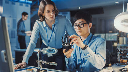 Technological Prosthetic Robot Arm is Tested by Two Professional Development Engineers in a High Tech Research Laboratory with Modern Futuristic Equipment. Man and Female Compare Data on a Personalの写真素材