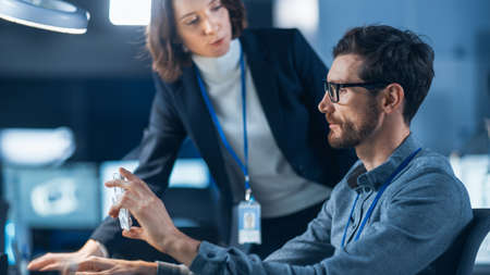 Futuristic Machine Engine Development Engineer Working on Computer at His Desk, Talks with Female...