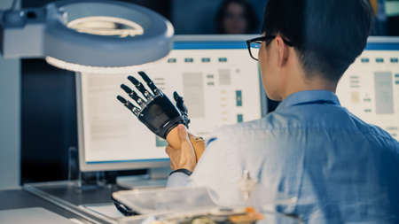 Close Up of a Futuristic Prosthetic Robot Arm Being Tested by a Professional Japanese Development Engineer in a High Tech Research Laboratory with Modern Computer Equipment.の写真素材