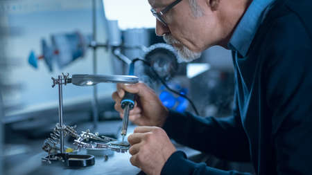 Portrait of Focused Middle Aged Engineer in Glasses Working with High Precision Laser Equipment, Using Lenses and Testing Optics for Accuracy Required Electronicsの写真素材