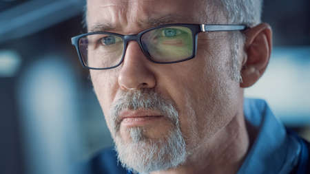 Close-up Portrait of the Handsome Middle Aged Man Wearing Glasses Working on Computer. Attractive Gray Haired Man with Blue Eyesの写真素材