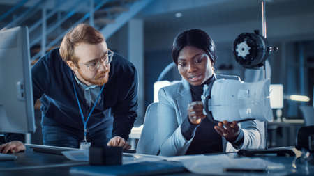 Electronics Development Engineer Working at His Desk, Talks with Project Manager, Shows Mechanism...