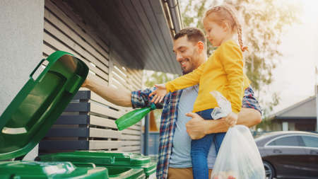 Father Holding a Young Girl and Throw Away an Empty Bottle and Food Waste into the Trash. They Use Correct Garbage Bins Because This Family is Sorting Waste and Helping the Environment.の写真素材