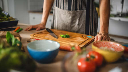 Close Up Shot of a Man and a Chopped Green Spring Onion on a Cutting Board. Preparing a Healthy Organic Salad Meal in a Modern Kitchen. Natural Clean Diet and Healthy Way of Life Concept.の写真素材