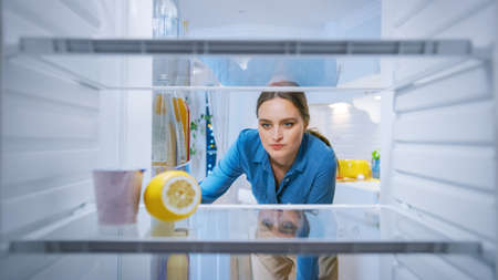 Dissappointed and Angry Young Woman Looks inside the Fridge, Checks Out that its Empy. Point of View POV from Inside of the Kitchen Refrigeratorの写真素材