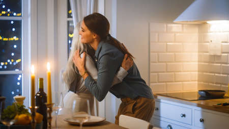 Beautiful Women Preparing and Serving Dinner in Kitchen. Elderly Mother Hugs Mature Daugher. THey Have Fun, Cooking Together, Talking, Gossip, Share Secrets and Recipes. Family Evening.の写真素材