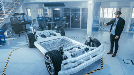 Automotive Engineer Working on Electric Car Chassis Platform, Using Augmented Reality Headset. In...