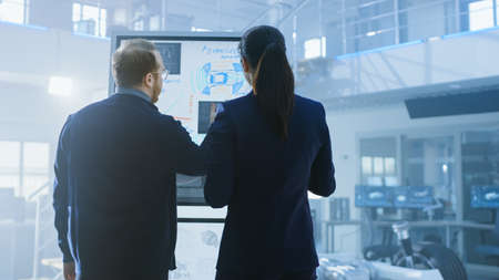 Male and Female Design Engineers are Working and Discuss Electric Car Benefits on an Interactive...