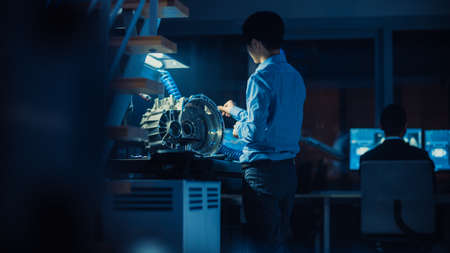 Professional Automotive Engineer in Glasses is Working on Transmission Gears in a High Tech Innovative Laboratory with a Computer Screens.の写真素材