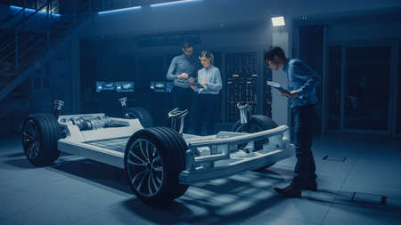 Diverse Automobile Engineers Talking while Working on Electric Car Platform Chassis Prototype. In Automotive Innovation Facility Concept Vehicle Frame Includes Tires, Suspension, Engine and Batteryの写真素材