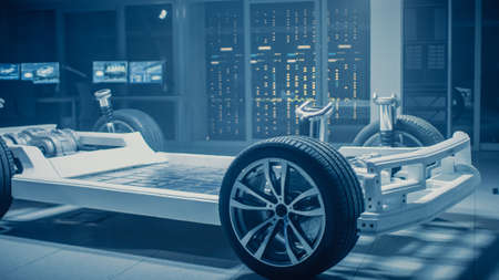 Automobile Engineers Discussing and Designing Electric Car Chassis Platform, Using Tablet Computers with 3D CAD Software. In Automotive Innovation Facility Vehicle Frame with Wheels, Engine andの写真素材
