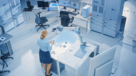 Stylish Female Industrial Robotics Engineer Looks at Blueprints Engineering Ways to Program and Manipulate Robot Arm for Lifting, Moving Objects. Technology Research Facility for Machine Learning and Stylish Female Industrial Robotics Engineer Looks at Blueprints Engineering Ways to Program and Manipulate Robot Arm for Lifting, Moving Objects. Technology Research Facility for Machine Learning and