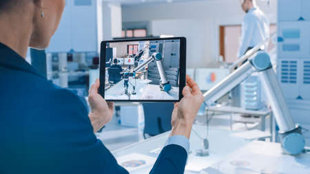 Stylish Female Industrial Robotics Engineer Uses Tablet Computer Recording a Video of Moving Robot Arm Used for Lifting, Moving Objects. Technology Research Facility for Machine Learning and Cloud Stylish Female Industrial Robotics Engineer Uses Tablet Computer Recording a Video of Moving Robot Arm Used for Lifting, Moving Objects. Technology Research Facility for Machine Learning and Cloud