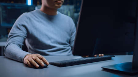 Portrait Shot of Anonymous Software Developer Sitting at His Desk and Working on Computer in Digital Identity Cyber Security Data Center. Hacking or Programming.の写真素材