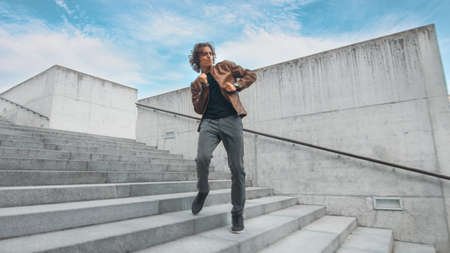 Cheerful and Happy Young Man with Long Hair Actively Dancing While Walking Down the Stairs. Hes...