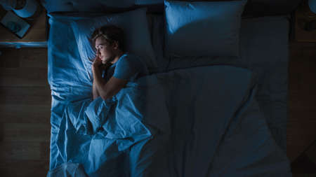Top View of Handsome Young Man Sleeping Cozily on a Bed in His Bedroom at Night. Blue Nightly Colors...