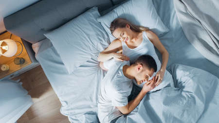 Happy Young Couple Cuddling Together in the Bed, Young Woman is Pregnant, Loving Partner Leans and Listens to a Baby Moving and its Heartbeat in the Belly. Tender and Loving Moments of Family Life.の写真素材