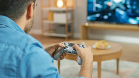 In the Living Room Man Sitting on a Couch Holds Controller Playing in a Console Video Game, 3D...