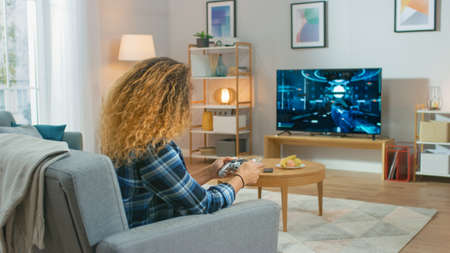 In the Living Room Girl Sitting on a Couch Holds Controller Playing in a Console Video Game, 3D...