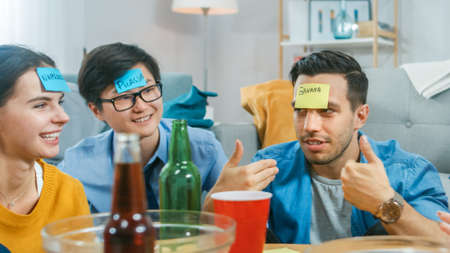 In the Living Room Diverse Group of Fun Loving Friends Playing Who am I game With Sticky Papers with...