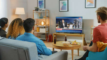 Happy Friends Sitting At Home Watching News. Relaxing on a Couch.right Cozy Apartment with Friends...