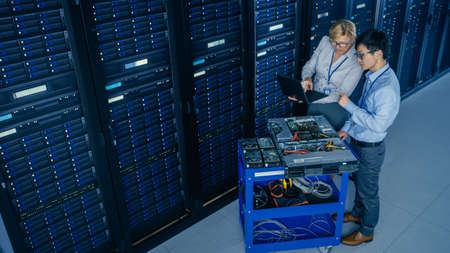 In the Modern Data Center: Engineer and IT Specialist Work with Server Racks, on a Pushcart...