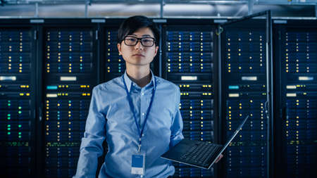 In the Modern Data Center: Portrait of IT Engineer Stand Near Server Racks, Finishing Maintenance...