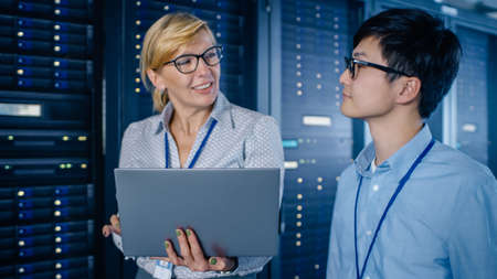 In the Modern Data Center: Engineer and IT Specialist Walking alongside Server Racks, Talking, Doing...