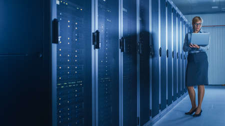 In Data Center: Female IT Technician Running Maintenance Programme on a Laptop, Controls Operational...