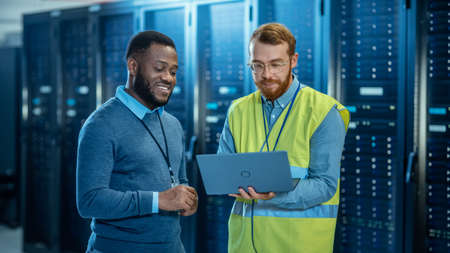 Bearded IT Specialist in Glasses and High Visibility Vest with a Laptop Computer and Black...
