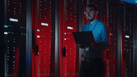 Angry Bearded IT Specialist in Glasses is Walking Through Server Rack Corridor in Data Center and...