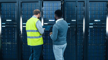 IT Administrator with a Laptop Computer in High Visibility Vest and Black Male Engineer are Talking...