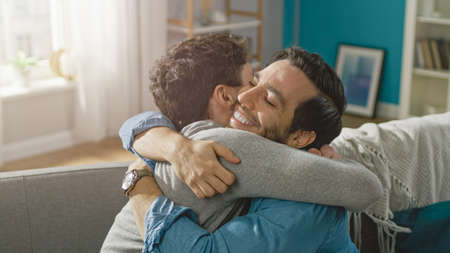 Cute Attractive Male Gay Couple Sit Together on a Sofa at Home. Boyfriends are Hugging and Embracing...