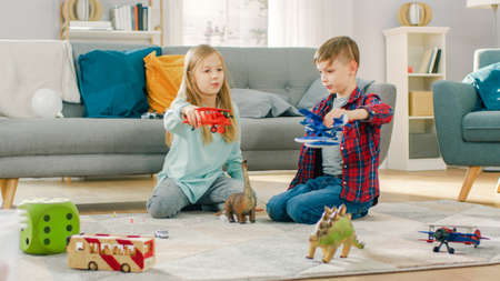 In the Living Room: Boy and Girl Playing with Toy Airplanes and Dinosaurs while Sitting on a Carpet. Sunny Living Room with Children Having Fun.の写真素材