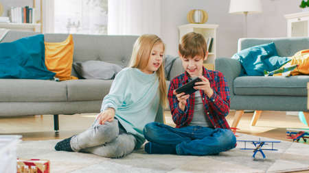 At Home: Cute Little Girl and Sweet Boy Playing Video Game on a Smartphone, Boy Holds Mobile Phone...