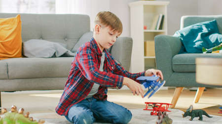 At Home: Smart Little Boy Plays with Toy Airplane. Young Child Playing on a Carpet in the Sunny Living Room.の写真素材