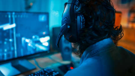 Close Up Back Shot of a Gamer Wearing a Headset with Mic and Playing Online Shooter Video Game on...