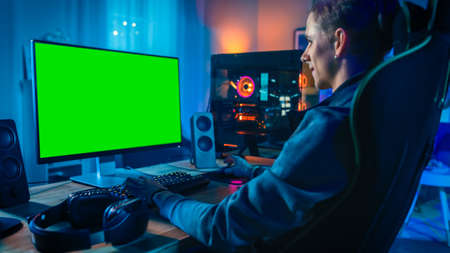 Excited Gamer Playing Online Video Game with a Mock Up Green Screen on His Powerful Personal...
