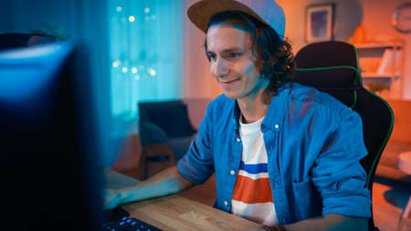 Excited Gamer in Cap Playing Online Video Game on His Personal Computer. Room and PC have Colorful...