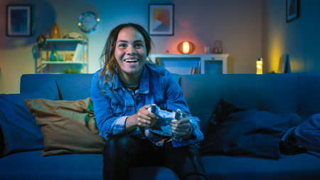 Beautiful Excited Young Black Gamer Girl Sitting on a Couch and Playing Video Games on a Console....