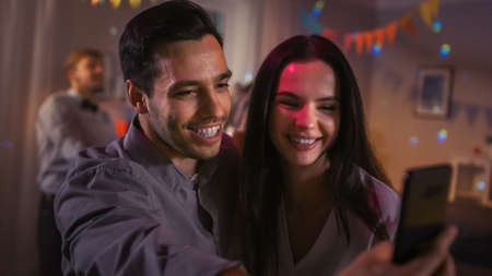 At the Wild House Party: Beautiful Young Couple Take Selfies with a Smartphone for Social Network...