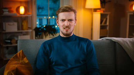 Portrait of a Handsome Man Sitting on a Couch at Home at Night, Watching Gore Horror Movie on TV. He...