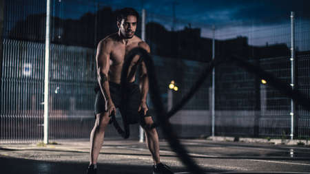 Strong Muscular Fit Shirtless Young Man is Doing Exercises with Battle Ropes. He is Doing a Workout...