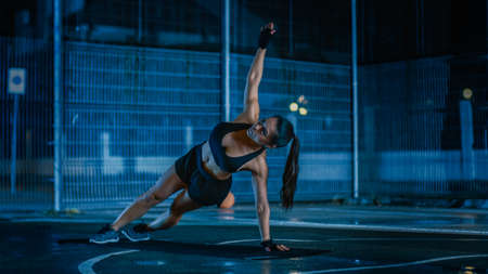 Beautiful Sporty Fitness Girl Doing Push Up Exercises. She is Doing a Workout in a Fenced Outdoor Basketball Court. Night After Rain in a Residential Neighborhood Area.の写真素材