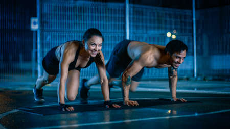 Smiling Happy Athletic Fitness Couple Doing Mountain Climber Exercises. Workout is Done in a Fenced Outdoor Basketball Court. Night After Rain in a Residential Neighborhood Area.の写真素材