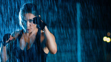 Beautiful Sporty Fitness Girl is Doing Sharowboxing Exercises. She is Ready to Punch. Workout at Night in Heavy Rain with One Light Behind Her.の写真素材