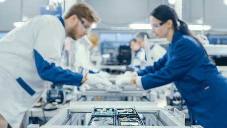 Shot of an Electronics Factory Workers Assembling Circuit Boards by Hand While it Stands on the Assembly Line. High Tech Factory Facility.の写真素材