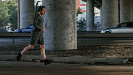 Athletic Young Man in Earphones and Sports Outfit is Jogging in the Street. He is Running in an...