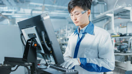 On High Tech Factory Asian Engineer Uses Computer for Programing Pick and Place Electronic Machinery for Printed Circuit Board Surface Mount Assembly Line. Production of PCB with SMT Machinery.の写真素材